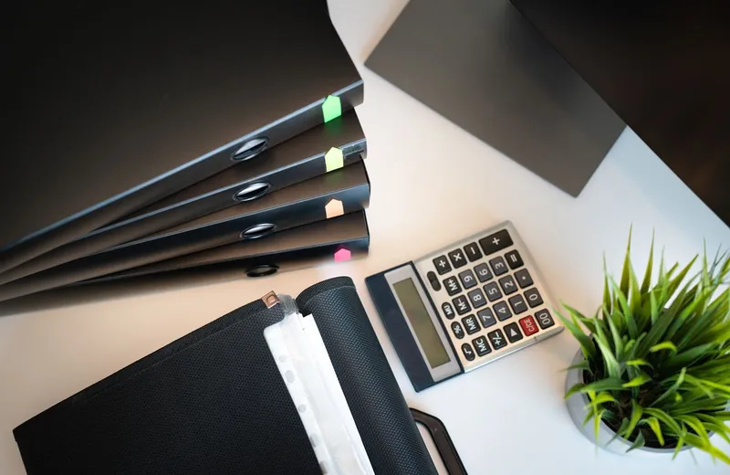 Ring binders tabbed in colour, stacked beside a calculator on a desk.