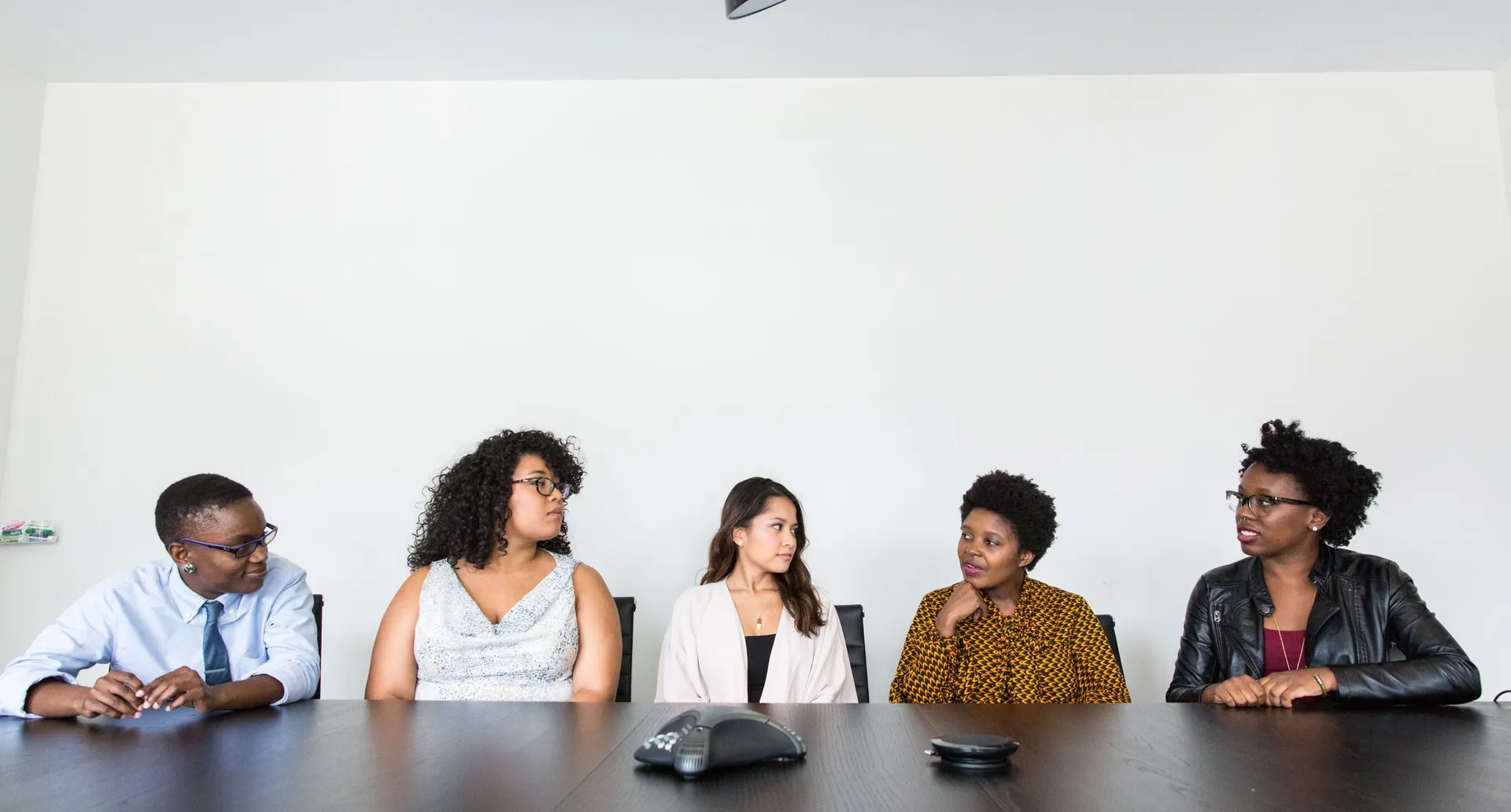 Five colleagues seated along one side of a boardroom table, turned toward each other in discussion.