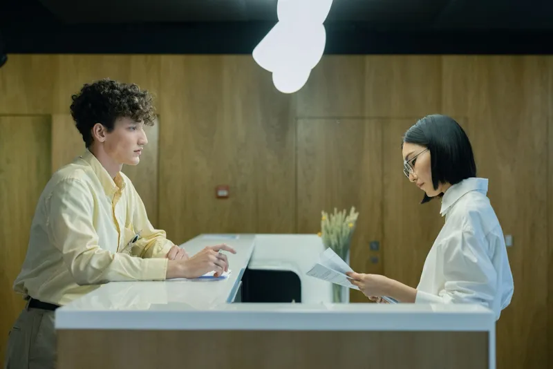 Two people either side of an office front desk, one passing a printed form across the counter.