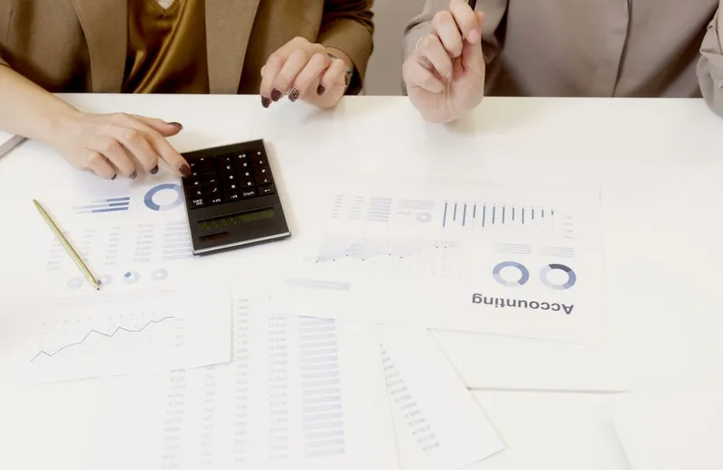 Two people at a desk working through printed statements with a calculator between them.