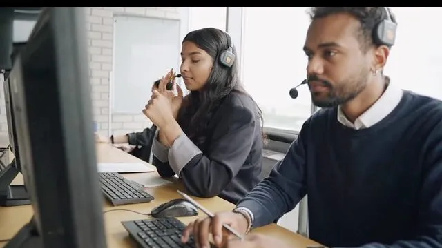 Two people at adjacent workstations, wearing headsets, working through queues on screen.